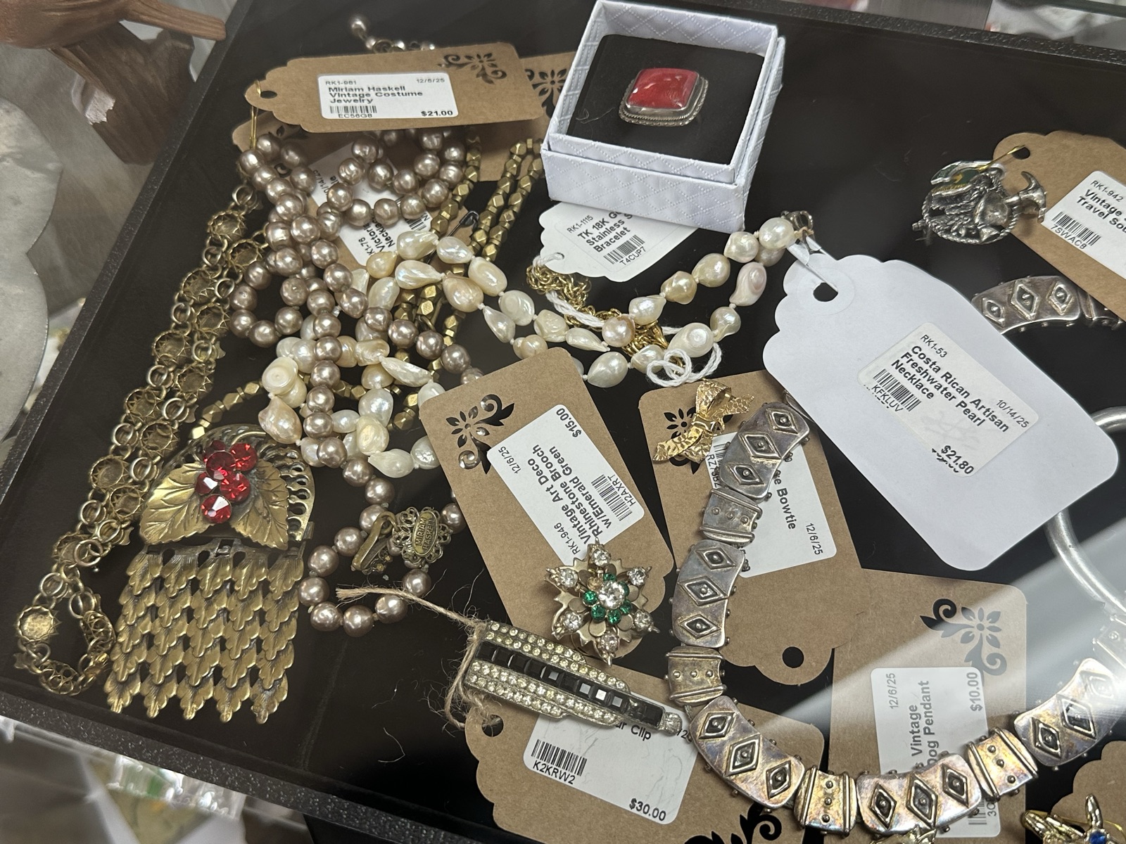 Assorted vintage jewelry including pearl necklaces, brooches, and rings in a glass display case