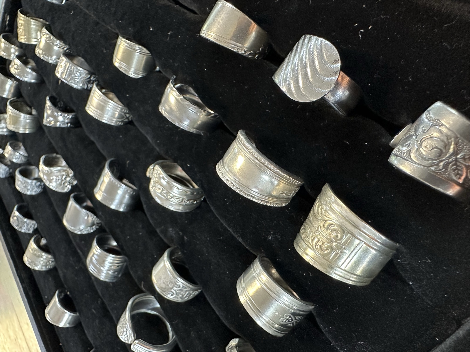 Rows of handmade sterling silver spoon rings on black velvet display by TS Designs