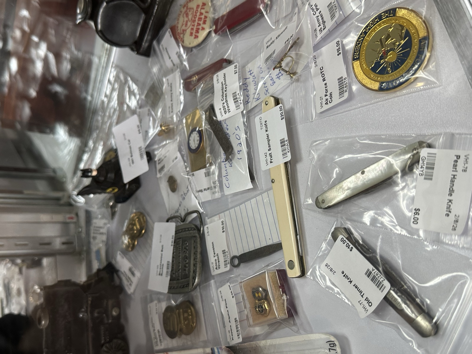 Collection of vintage pocket knives, pins, and small collectibles in a glass display case