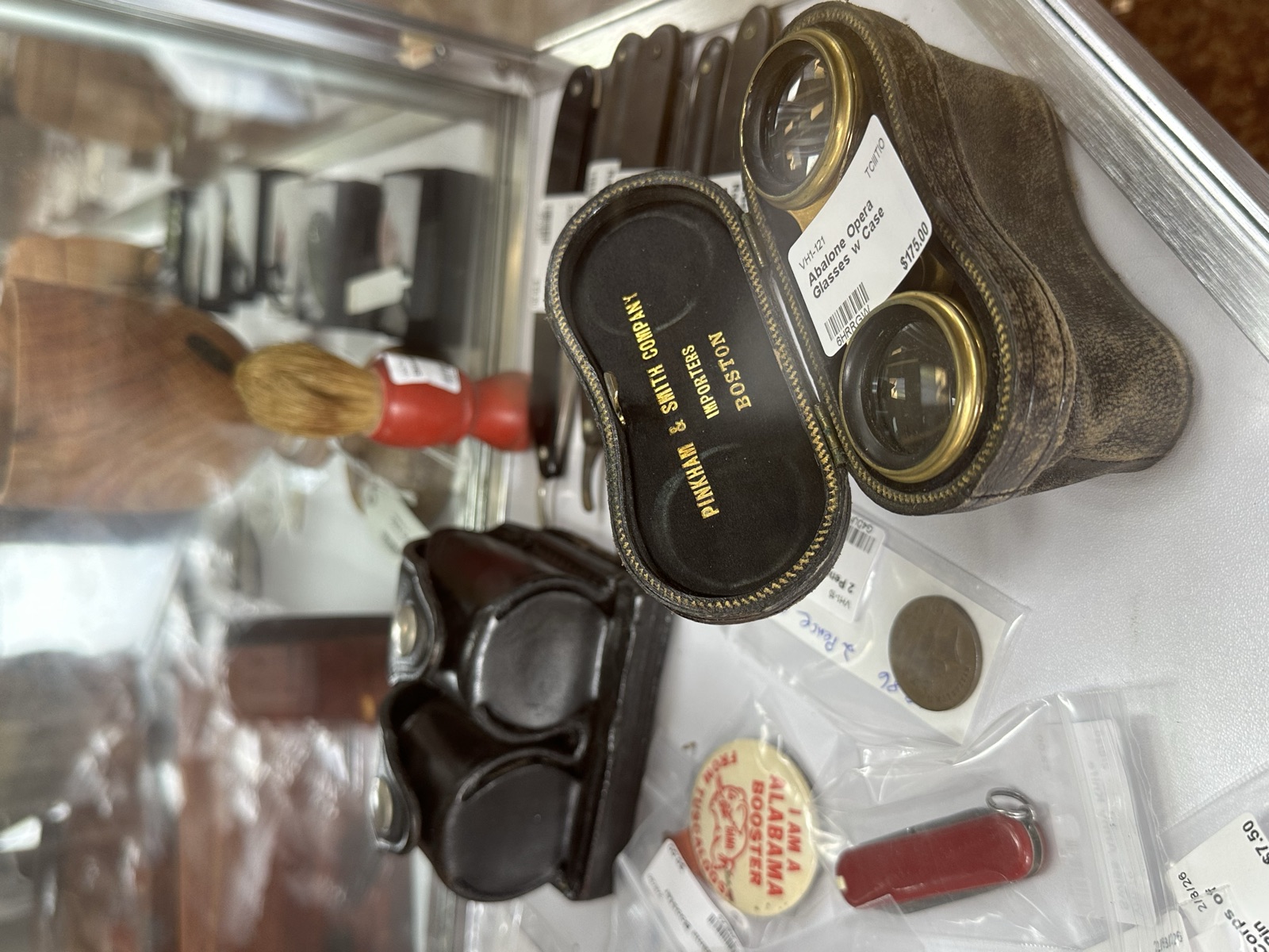 Vintage binoculars, brushes, and small antique items in a glass case