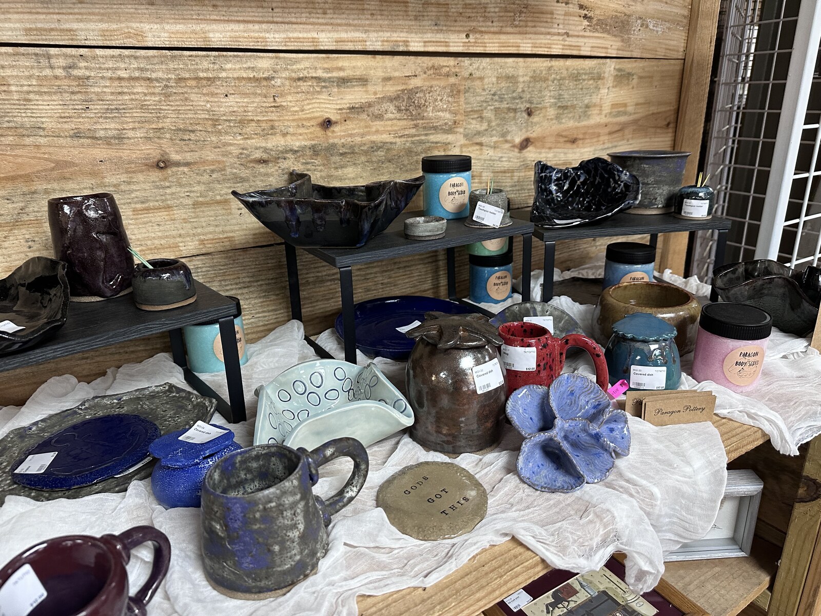 Paragon Pottery booth inside Triangle Trading Post with glazed mugs, bowls, plates, and body scrub jars